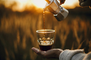 Hipster pouring fresh hot coffee from geyser coffee maker into glass cup in sunny warm light in...