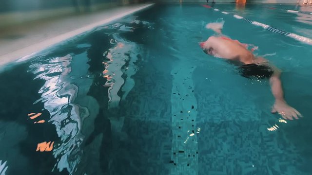 Gimbal shot go pro slow motion of professional swimmer crawling in swimming pool. Professional swimmer in goggles swimming fast training in the pool