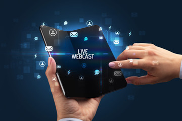 Businessman holding a foldable smartphone with LIVE WEBCAST inscription, social networking concept