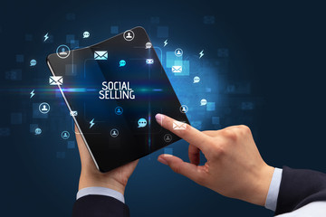 Businessman holding a foldable smartphone with SOCIAL SELLING inscription, social networking concept