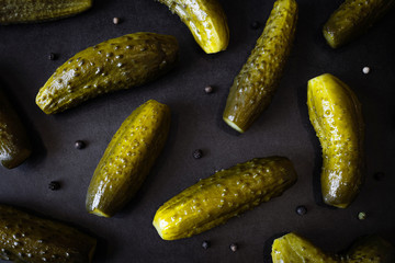 Pickled cucumbers and peppercorns lie on a dark background. The concept of fermented food. Flat lay, top view, copyspace.