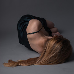 thin caucasian girl with long brown hair in dress lies on gray floor with her head turned away....
