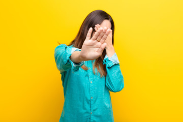 young pretty woman covering face with hand and putting other hand up front to stop camera, refusing...
