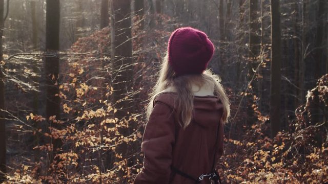 Young woman enjoying warm sun rays in autumn golden forest. Looking around and smiling feeling the weather.