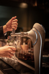 Close up chrome tap bartender holding a glass during pouring cold draft beer from dispenser, selective focus, background copy space, night time