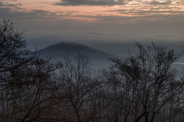 Obraz premium A cloudy and foggy sunrise looking over the valley below. A cold winter morning with the rolling hills in the background.