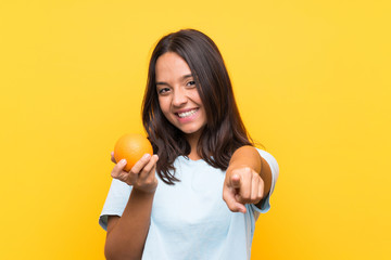 Fototapeta na wymiar Young brunette woman holding an orange points finger at you with a confident expression