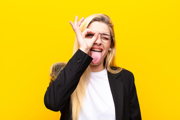young pretty blonde woman smiling happily with funny face, joking and looking through peephole,...