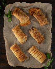 Baked puff pasrty with different fillings and herbs on baking paper or parchment on dark wooden background. Top view