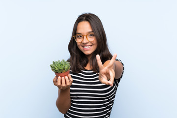 Young brunette woman holding a plant smiling and showing victory sign