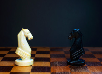 Old wooden chessboard with a white and black horse with copy space. Chess game, duel, intellectual game, strategy.