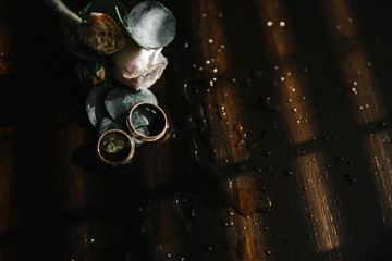 Beautiful toned picture with wedding rings lie on a wooden surface against the background of a bouquet of flowers