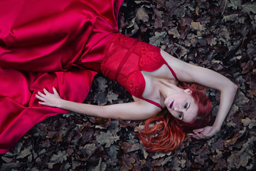 beautiful girl lie on a ground in red dress. dramatic dark fairytale forest