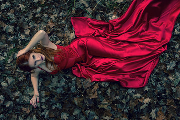 beautiful girl lie on a ground in red dress. dramatic dark fairytale forest