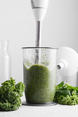 Cooking green smoothie in a blender on a light background. Close up. Fresh green smoothie in a blender. Top view. Freshly prepared vegetarian smoothies from shpenata cabbage and kale.