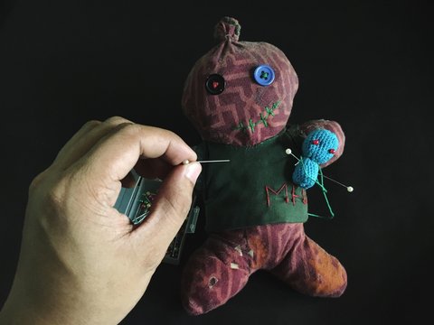 Cropped Hand Of Man Putting Straight Pin In Voodoo Doll Over Black Background
