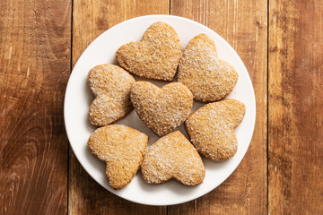 Heart shaped shortbread cookies lie on a white plate. The plate stands on a wooden table.