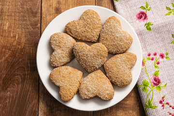 Heart shaped shortbread cookies lie on a white plate. The plate stands on a wooden table.