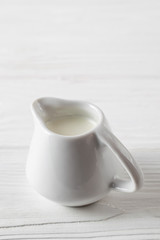 Small white ceramic milk jug on white wooden background
