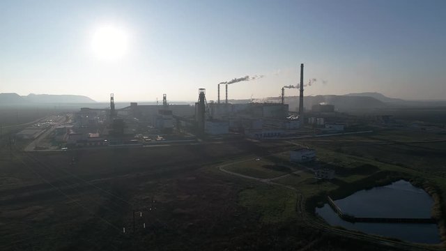Potash plant for the extraction of potash fertilizers, mountains of waste near the plant, smoke from pipes, shooting from a height, left flight