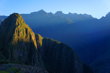 Fototapeta premium The sun breaks over the mountains and shines its first light on Machu Picchu mountain