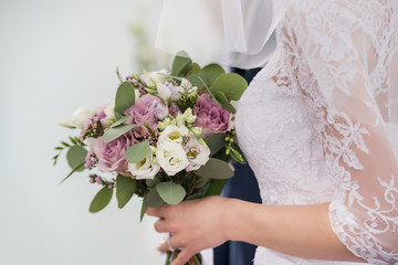 Bride hand holds stylish bridal bouquet with white and pink tenderness roses decorated eucaliptus leaves closeup