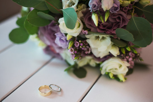 Wedding rings on white wooden surface and a bridal bouquet