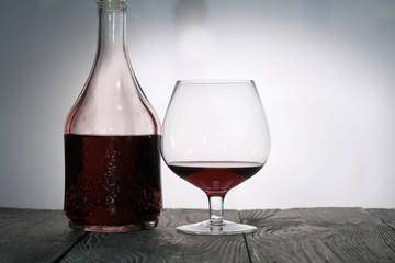 A glass of dry red wine. Bottle of wine. Stand on wooden boards. Shot in backlight.
