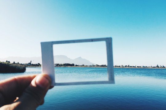 Cropped Image Of Hand Holding Picture Frame Against Sea