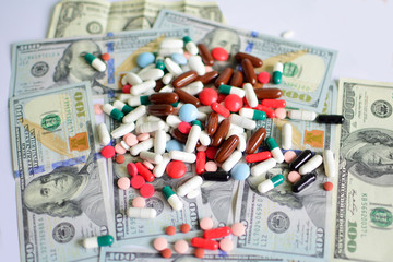 Pills of different colors next to american dollars. Expensive medicine. Cost of the healthy life. Medical insurance. Drug addiction. Money and pills.