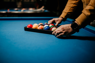 A men preparing pool balls in triangle. Blue billiard table