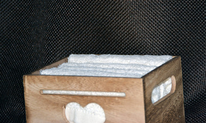 Wooden box for white towels. Face towel. Skin care. White towels in a wooden box on a brown background.