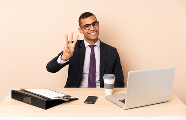 Young business man in his office with a laptop and other documents happy and counting three with fingers