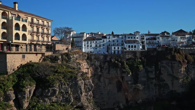 Gimbal pan shot left to right of Ronda city in Spain under bright sky in january. Old houses on the cliff, ronda cliff edge city and panorama view of green fields
