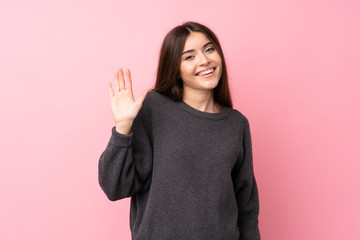 Young woman over isolated pink background saluting with hand with happy expression