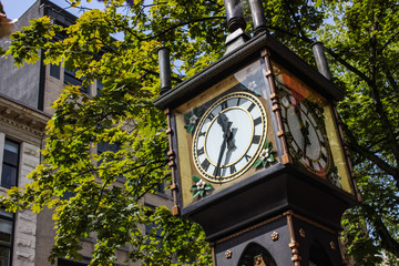 Gastown steam clock in Vancouver. Horizontal detailed close up with green leafs behind it.