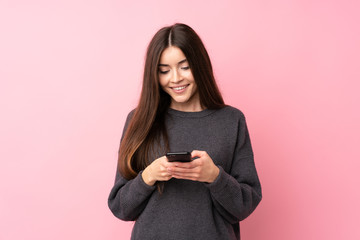 Young woman over isolated pink background sending a message with the mobile