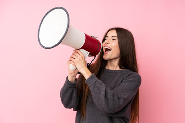Young woman over isolated pink background shouting through a megaphone - obrazy, fototapety, plakaty