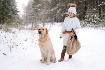 a little girl in white knitted clothes walks in the forest with her dog Labrador. looking for game or tree for home