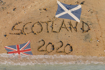 Scotland 2020 in Sand geschrieben mit schottischer Flagge und Union Jack