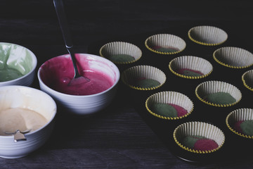Colored cupcake dough is poured into a mold.
