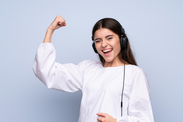 Young woman over isolated blue background using the mobile with headphones and dancing