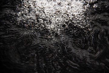 Fototapeta premium Water splash on a black background. Bubbles from the water. Interesting abstract water background against black background