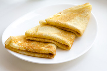 Three pancakes lie on a white plate on a white background. Selective focus. Close up.
