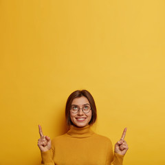 Vertical image of attractive smiling woman points index fingers above, brags about her new ceiling,...