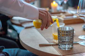 A waiter pours orange juice into a glass. Concept: service or food and drink