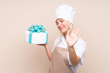 Young Russian woman with a big cake over isolated background saluting with hand with happy expression