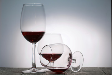 Glasses with red dry wine. One of them lies on its side with the remains of wine. Stand on wooden boards. Shot in backlight.
