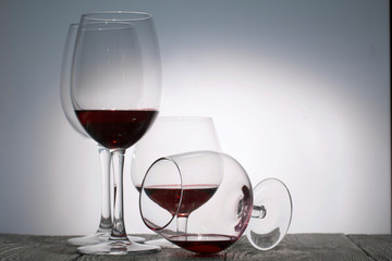 Glasses with red dry wine. One of them lies on its side with the remains of wine. Stand on wooden boards. Shot in backlight.