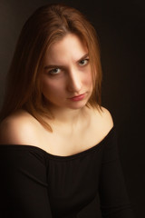 Fototapeta premium Portrait in the photo Studio of brown-haired girl, on a black background in black clothes with open shoulders. Short hair.